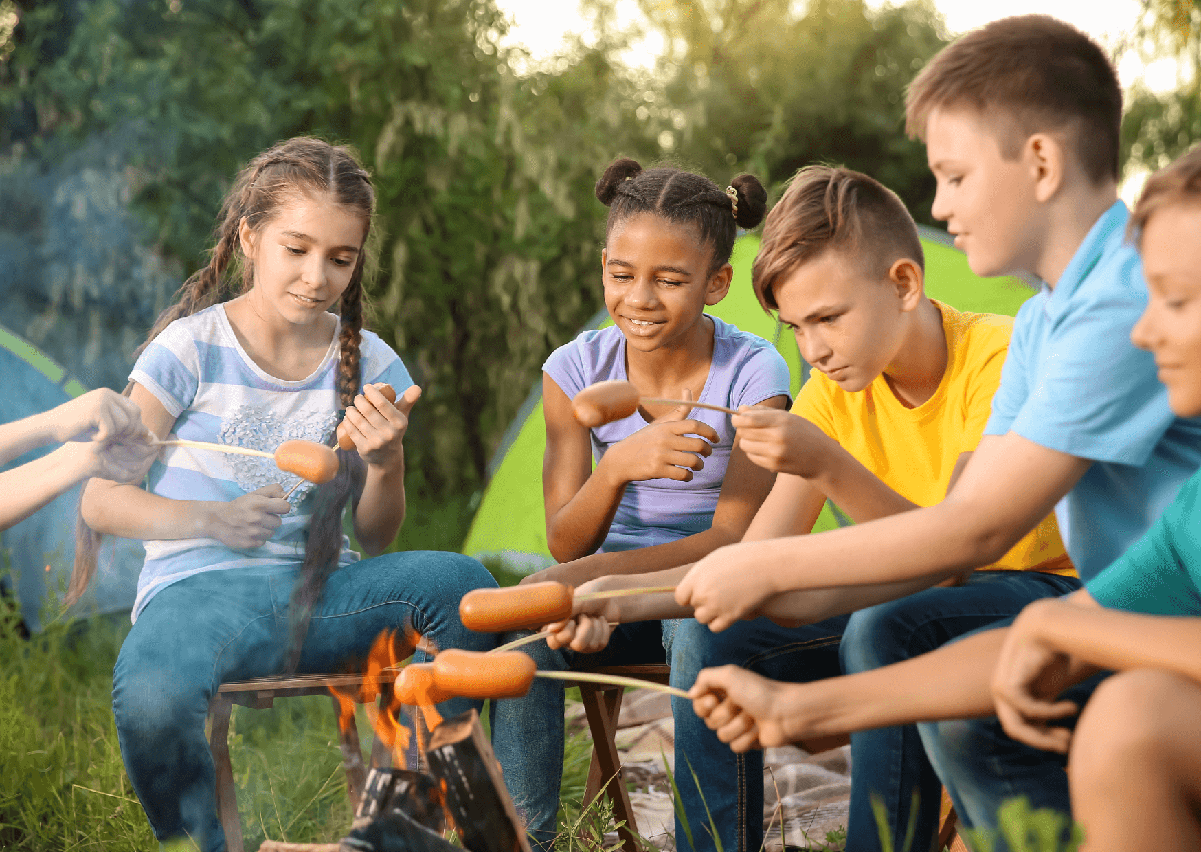 Auf geht's in die Natur - Angebote für Kinder von Oliver Eyth - Vier Jugendliche sitzen am Feuer und grillen Würstchen
